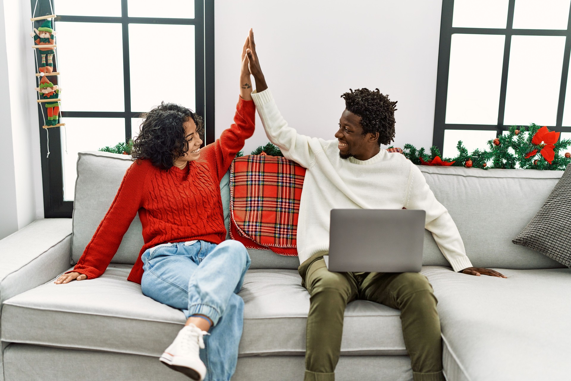 Young interracial couple using laptop and high five sitting on the sofa by at home.